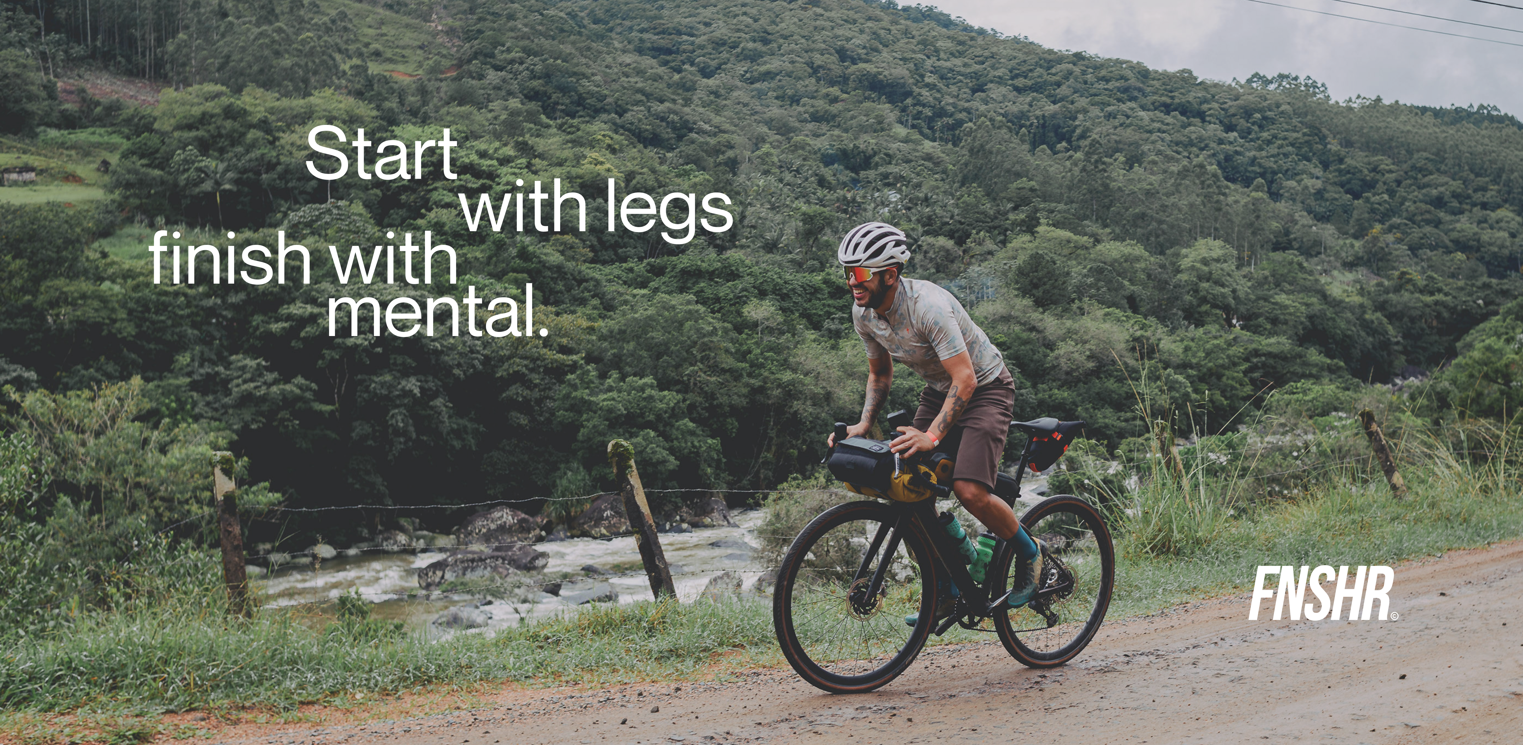 Cycliste sur un vélo de gravel roulant sur un chemin de terre en pleine nature, accompagné du slogan FNSHR : Start with legs, finish with mental.